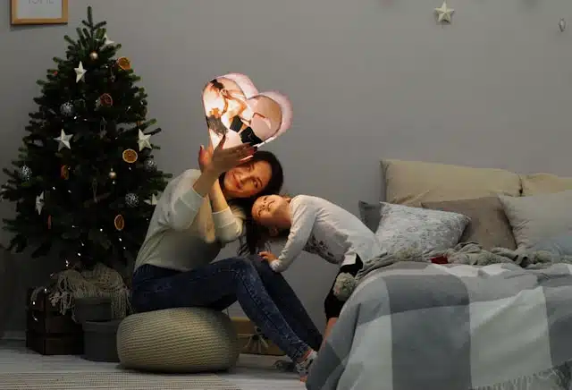 A young mother and daughter playing beside a Christmas tree in their home. 