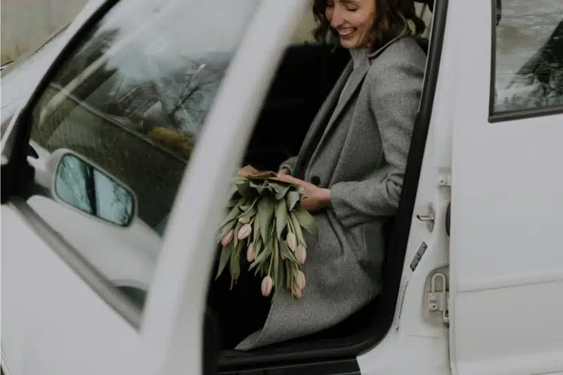 A woman smiling as she exits her vehicle holding flowers.